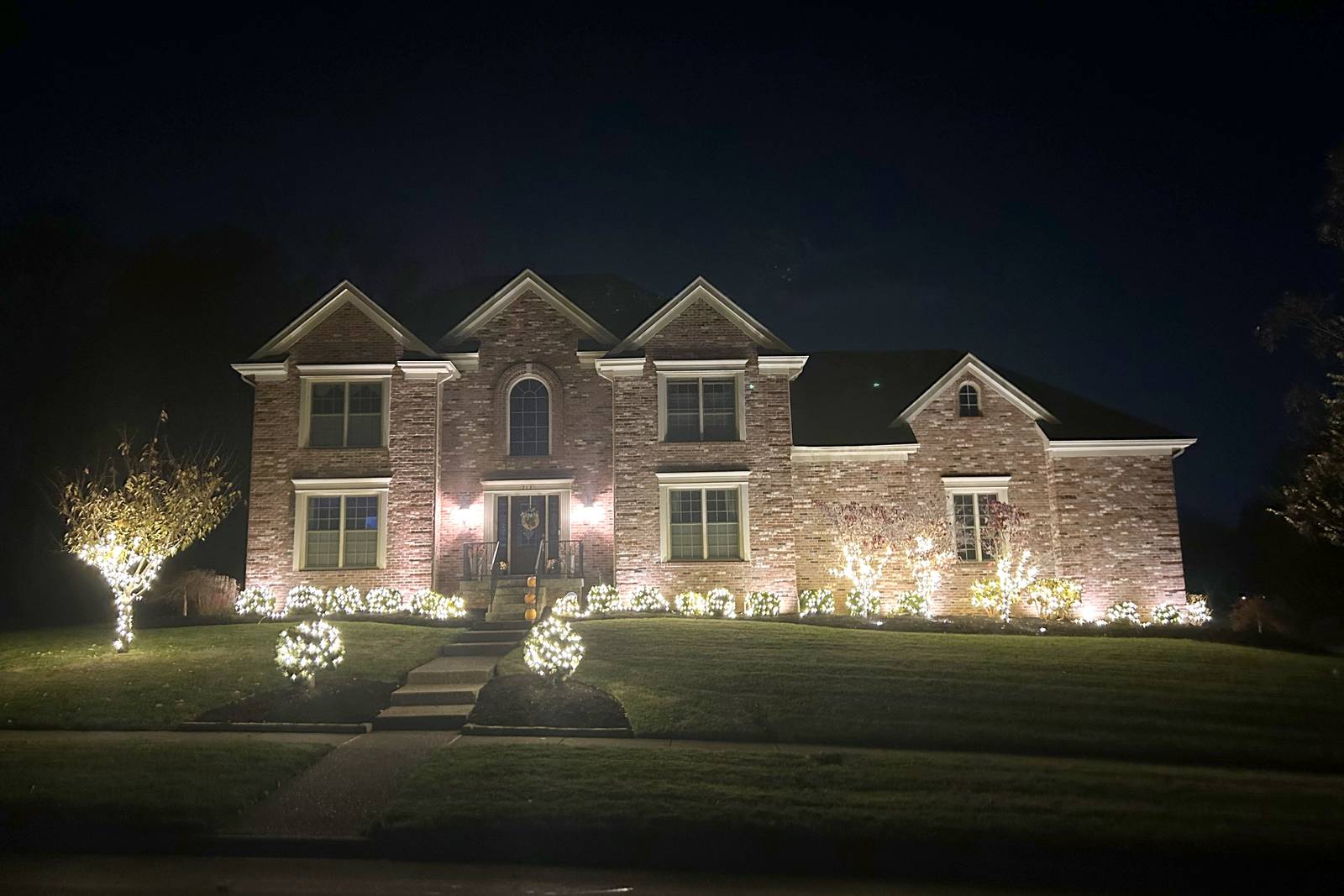 Brick colonial home with lit bushes and wrapped Christmas trees in Barbourmeade, Kentucky