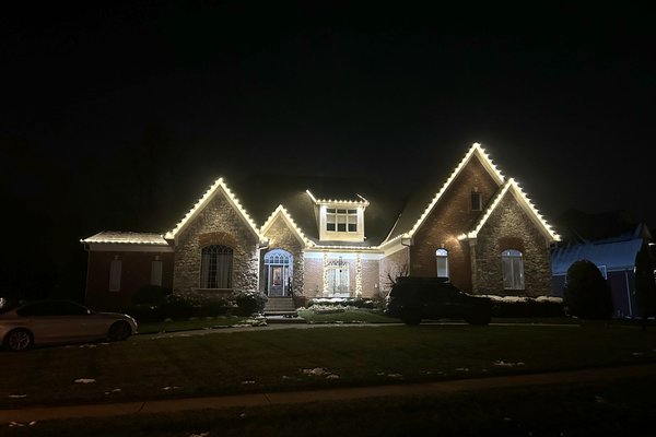 Warm white C9 Christmas lights along the roofline of a stone two-story home in Middletown, Kentucky