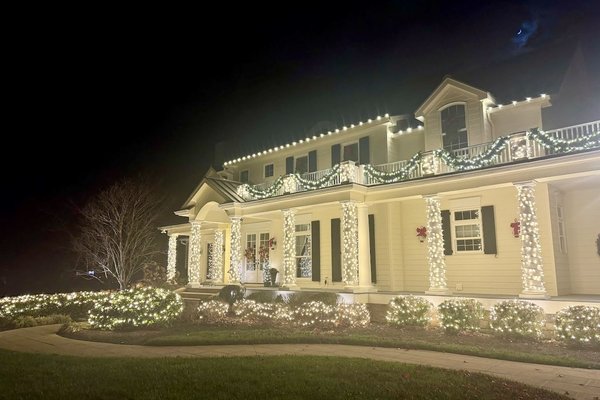 Lit garland wrapped around entry columns and wreaths on a white colonial home in Middletown, Kentucky